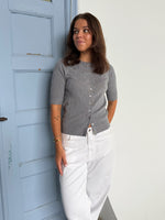 Modelfoto af pige som bærer en Spina cardigan i grå, samt et par hvide Nanna jeans. Alt fra By Sofie Sønderby