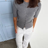 Modelfoto af pige som bærer en Spina cardigan i grå, samt et par hvide Nanna jeans. Alt fra By Sofie Sønderby