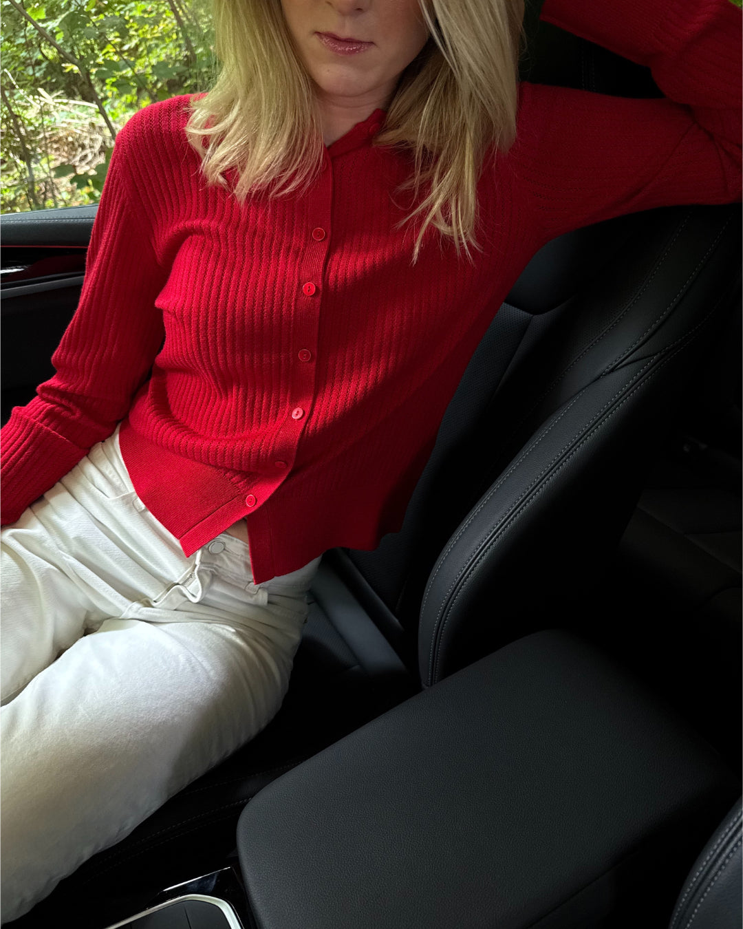 Modelfoto af pige i en rød Spina cardigan og hvide Nanna jeans. Alt er fra BySofieSønderby
