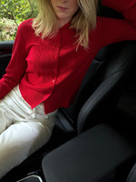 Modelfoto af pige i en rød Spina cardigan og hvide Nanna jeans. Alt er fra BySofieSønderby