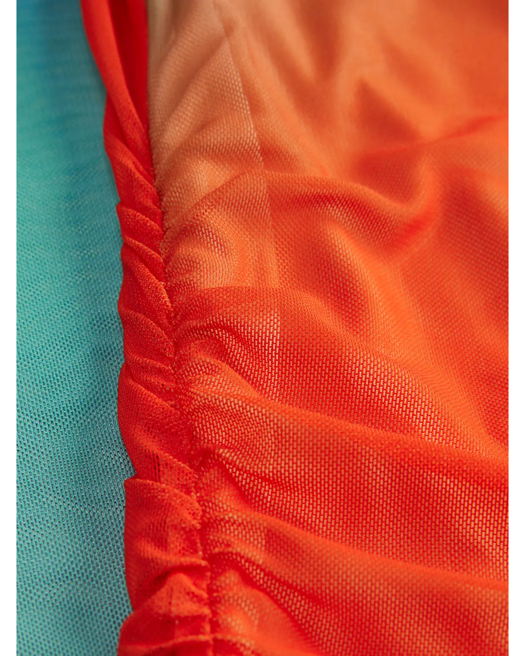 Orange og turkis stof folder sig elegant og glat sammen, hvor det ene stof har en ruched tekstur. Den lyse farvekontrast skaber et iøjnefaldende miks af nuancer.