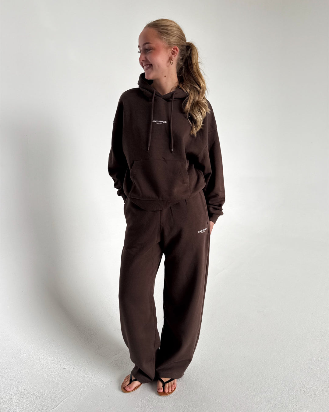 Modelfoto af pige som bærer en Studio Vesterbro hoodie i brun, samt Studio Vesterbro bukser i brun. Alt fra By Sofie Sønderby
