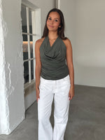 Modelfoto af pige som bærer en kakifarvet TAYLOR halterneck top, samt en hvide jeans. Alt er fra BySofieSønderby