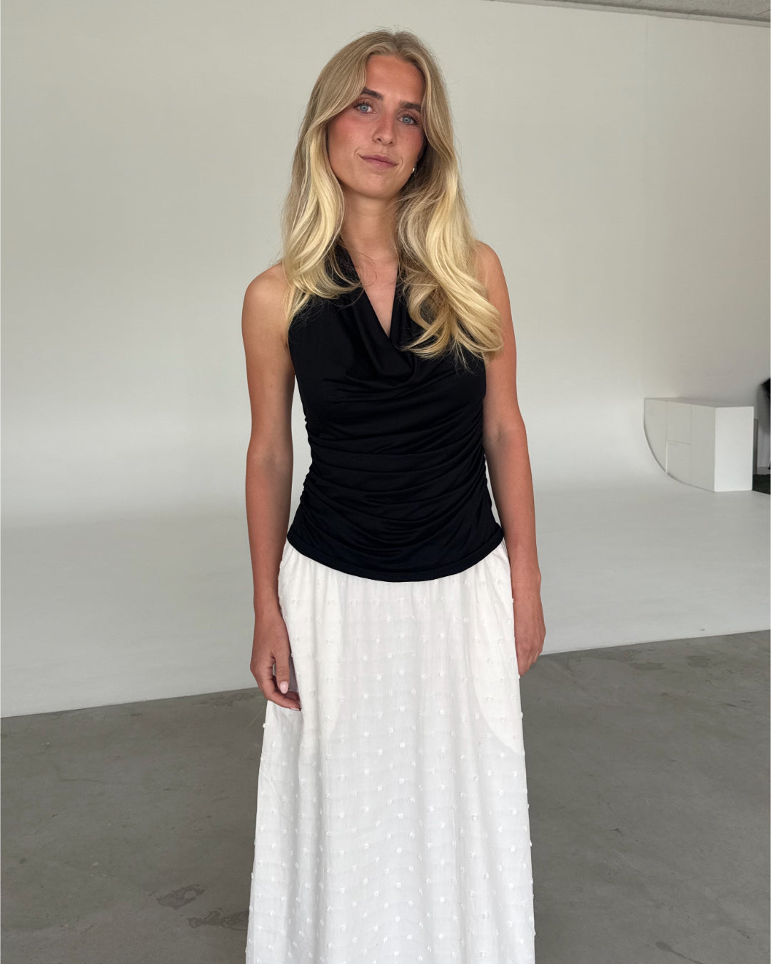 Modelfoto af pige som bærer en sort TAYLOR halterneck top, samt hvid nederdel. Alt er fra BySofieSønderby