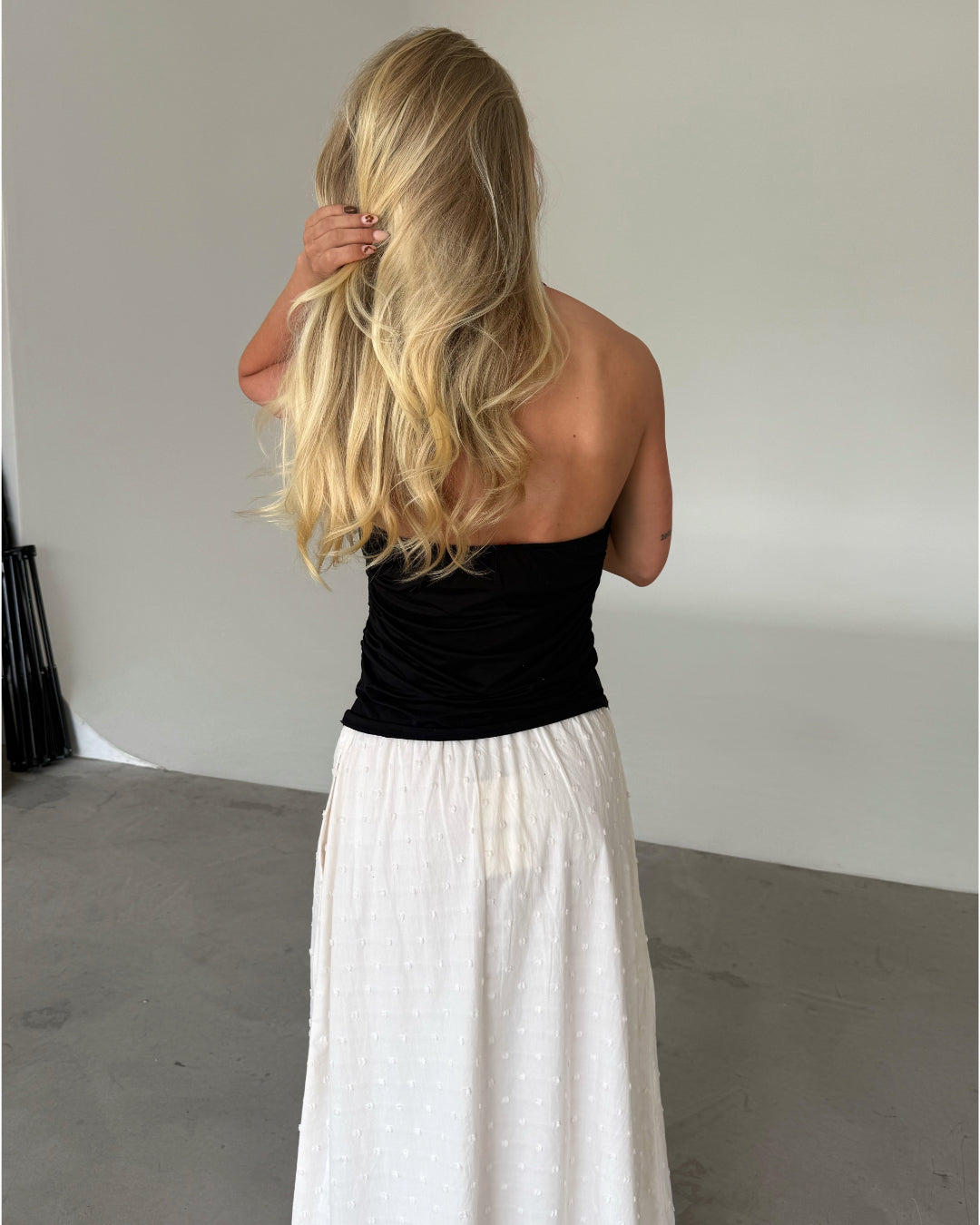 Modelfoto af pige som bærer en sort TAYLOR halterneck top, samt hvid nederdel. Set bagfra. Alt er fra BySofieSønderby