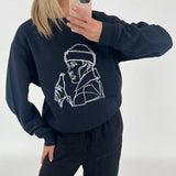 En person tager et spejlbillede iført en sort sweatshirt med en line-tegning af en person med en drikkeflaske. Baggrunden er neutral og lys.