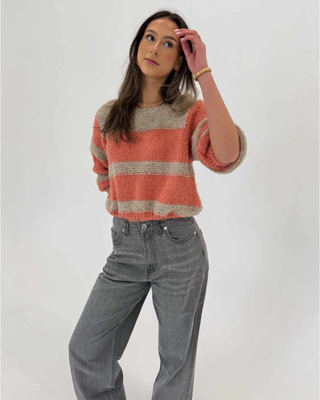 En person iført en stribet sweater og grå jeans står afslappet, mens de kigger opad i et lyst miljø.