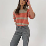 En person iført en stribet sweater og grå jeans står afslappet, mens de kigger opad i et lyst miljø.