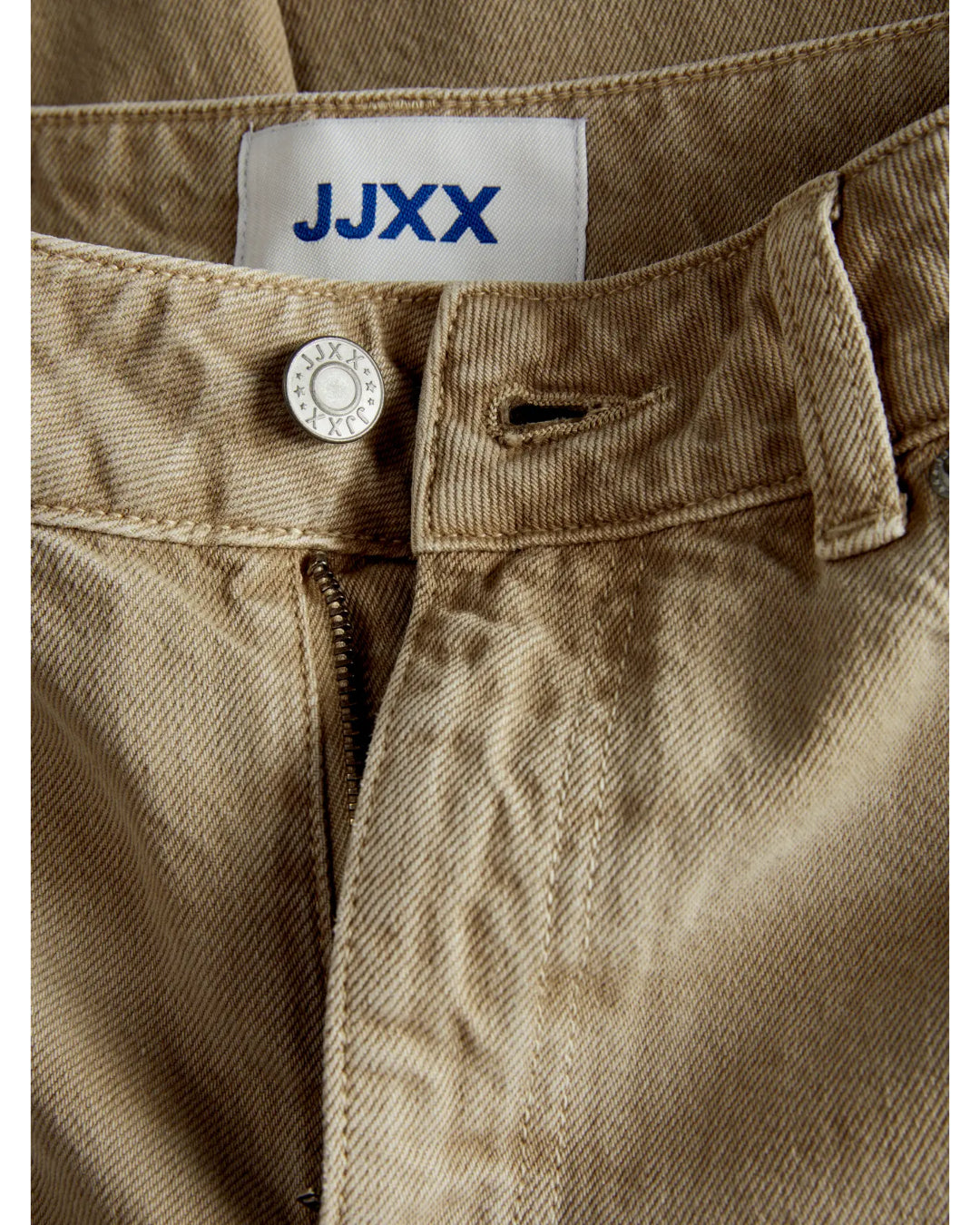 Knappen på et par beige bukser med lynlås er åben. Et mærke med teksten "JJXX" er synligt på indersiden.