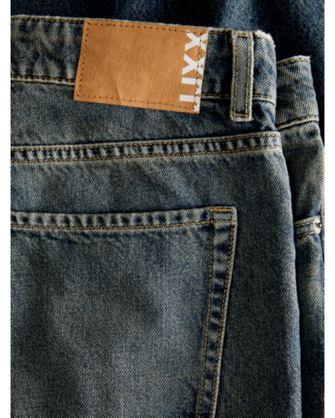 Et par blå jeans ligger fladt, med en brun læderlignende lap påsyet i taljen. På lappen står teksten "LXX". Jeansene har en tydelig synlig baglomme.
