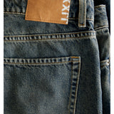 Et par blå jeans ligger fladt, med en brun læderlignende lap påsyet i taljen. På lappen står teksten "LXX". Jeansene har en tydelig synlig baglomme.