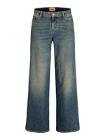 Jeans med bredt snit står oprejst mod en hvid baggrund. De har en lysere blå vask ved lårene og lommer foran. Text på linningen: "JXX".