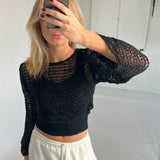 En person tager et spejlfoto med en smartphone og dækker sit ansigt. Personen bærer en sort netbluse og hvide bukser i et lyst rum.