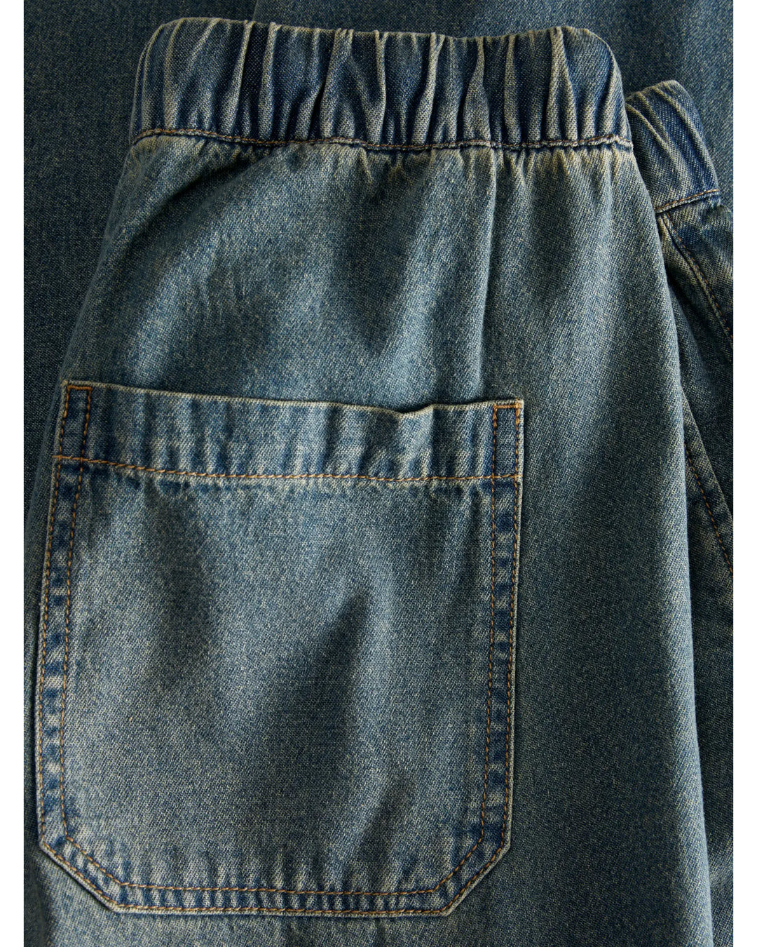 Baglomme af denimshorts med elastisk talje ses tæt på, viser denimvævningens blå farve og robuste syninger i et enkelt, afslappet design.
