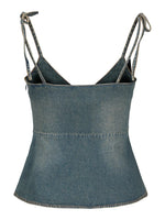 En denim-top med tynde stropper, der er bundet i knuder ved skuldrene. Toppen har enkle syninger og fremstår i et lysblåt dongeristof.