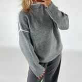 En person iført en grå sweater med hvide striber tager et spejlselfie med en smartphone, omgivende enkle og ensfarvede baggrund.
