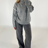 Person iført en løs, grå sweater og vide, mørkegrå bukser står i et minimalistisk rum, tager et spejlbillede med en smartphone.