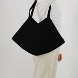 Sort taske bæres over skulderen af person i hvid skjorte og beige bukser; skaber en elegant og minimalistisk stil i neutral baggrund.