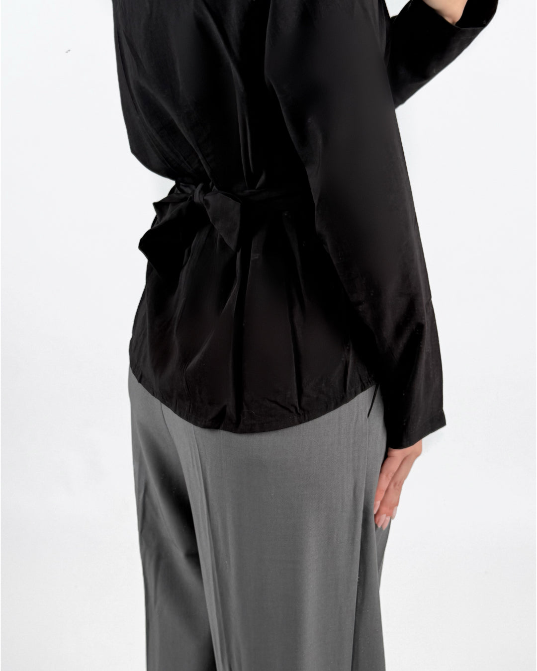 Modelfoto af pige med sort YUI bluse med sløjfedetalje på ryg, samt grå MILAN bukser. Set bagfra. Alt er fra BySofieSønderby