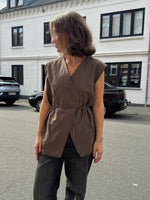 Modelfoto af pige i brun Yui vest med bindebånd, samt grå Nanna jeans. Alt er fra BySofieSønderby