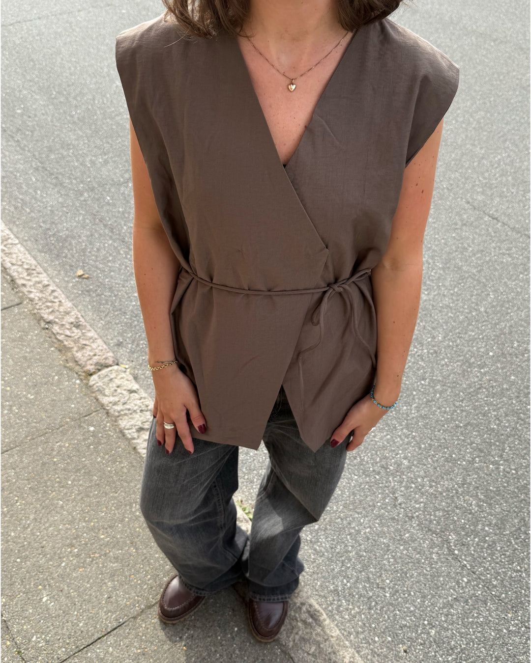 Modelfoto af pige i brun Yui vest med bindebånd, samt grå Nanna jeans. Alt er fra BySofieSønderby