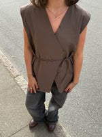Modelfoto af pige i brun Yui vest med bindebånd, samt grå Nanna jeans. Alt er fra BySofieSønderby