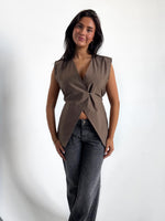 Modelfoto af pige i brun Yui vest med bindebånd, dertil grå Nanna jeans. Alt er fra BySofieSønderby