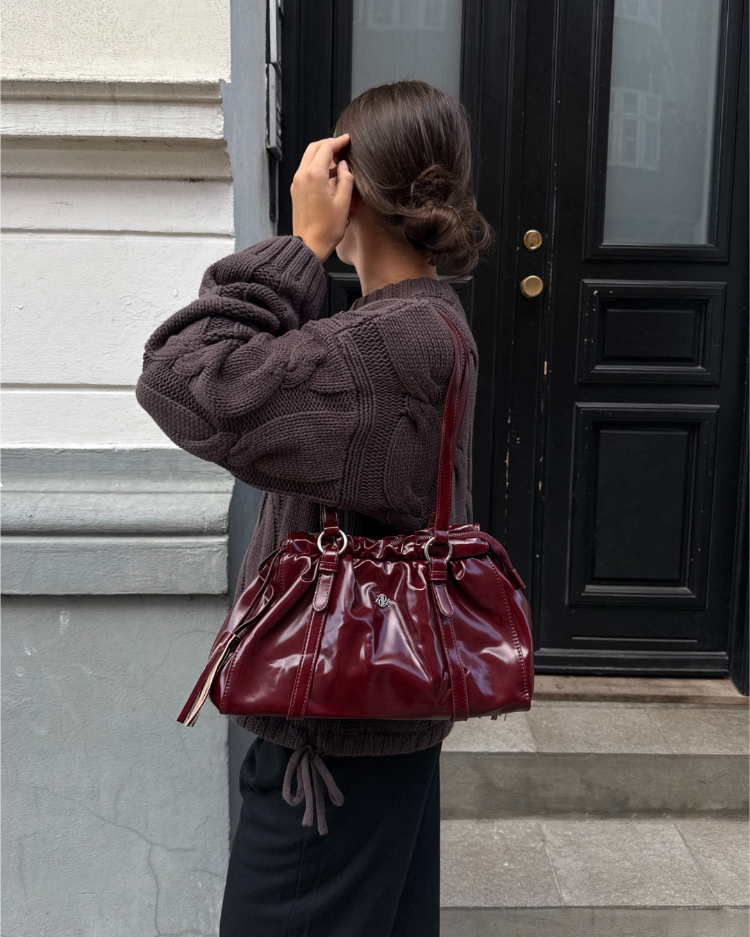 Modelfoto af pige med bordeaux Zahra taske på skulderen. Hun er iført sorte bukser og brun Bay striktrøje. Alt er fra BySofieSønderby