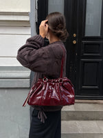 Modelfoto af pige med bordeaux Zahra taske på skulderen. Hun er iført sorte bukser og brun Bay striktrøje. Alt er fra BySofieSønderby