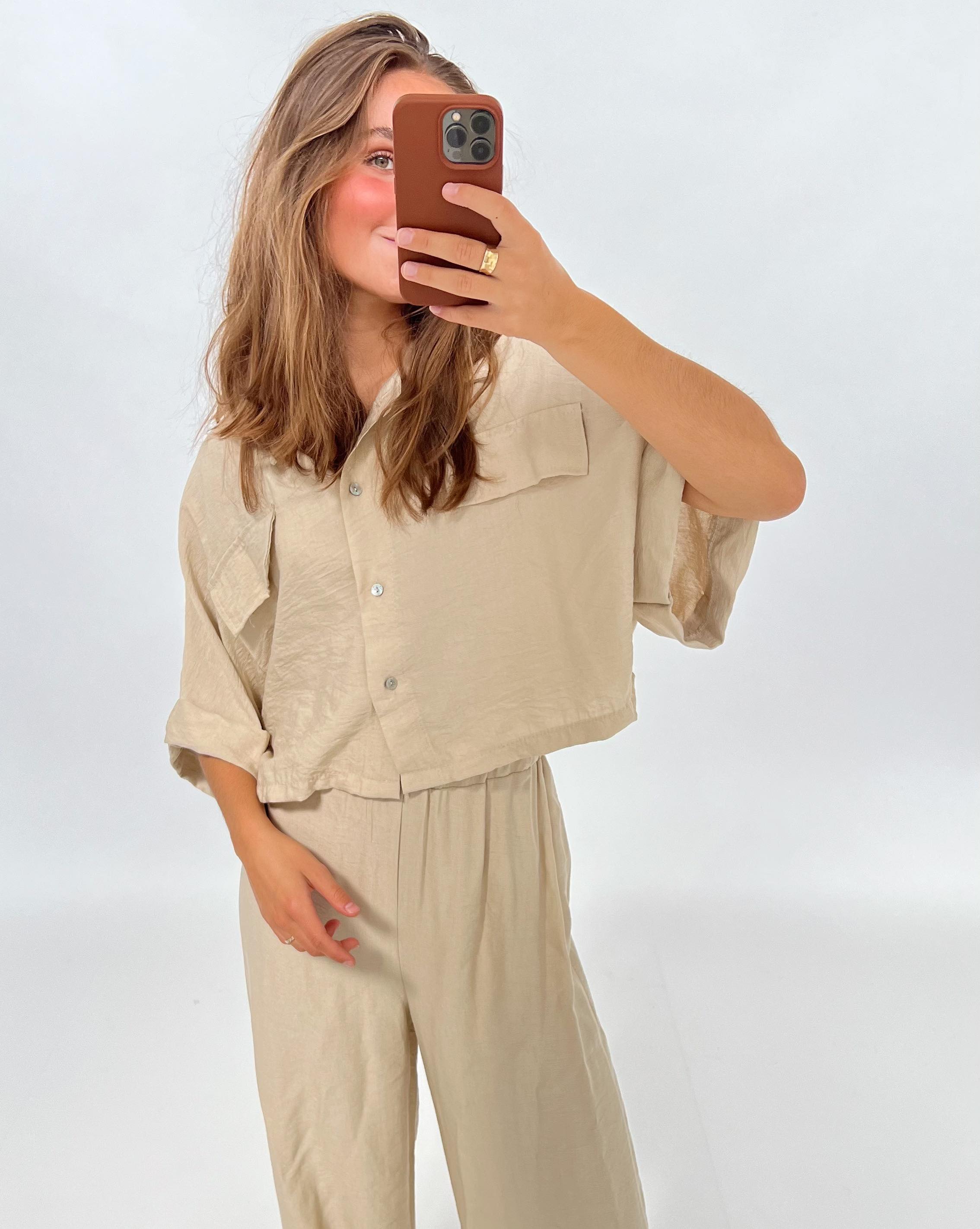 En person iført en lys, løs dragt tager et spejlbillede med en smartphone i en minimalistisk, lys baggrund.