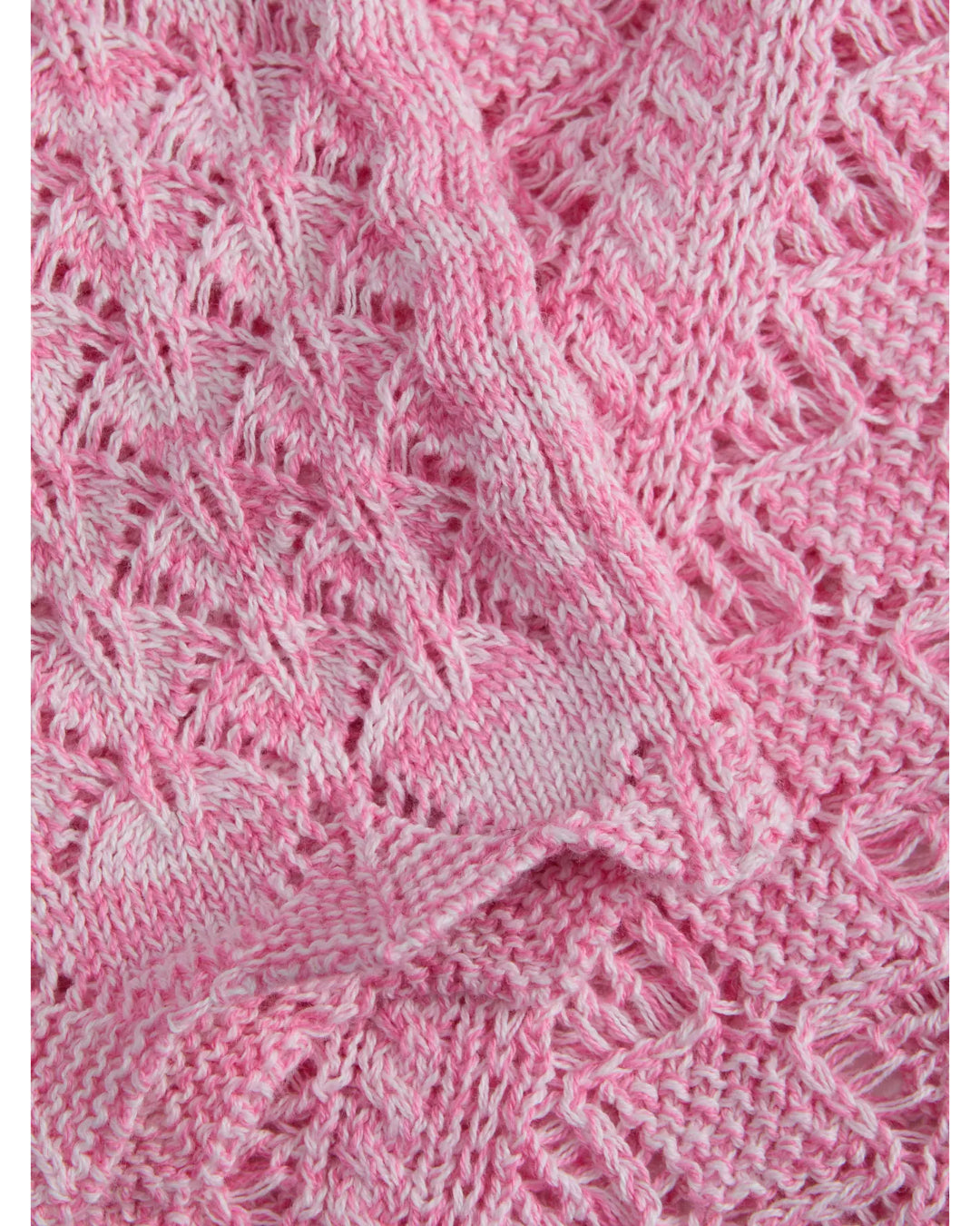 Strikket tekstil i pink med lyse mønstre, ligger udfoldet i lag med en struktureret, blød overflade.