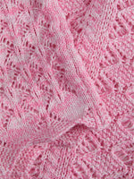 Strikket tekstil i pink med lyse mønstre, ligger udfoldet i lag med en struktureret, blød overflade.