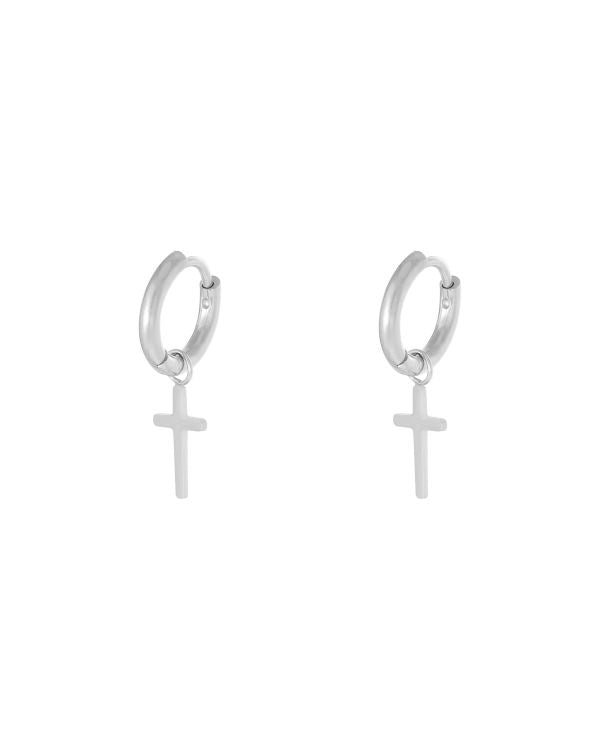 To sølvøreringe med korsvedhæng hænger mod en hvid baggrund, mens de afspejler lys og udstråler et enkelt, elegant design i et minimalistisk miljø.