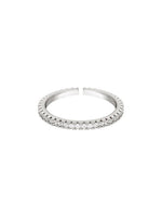 En åben sølvring med indlagte, klare sten langs kanten, ligger centralt mod en hvid baggrund. Ringen er glitrende og elegant i sit design.