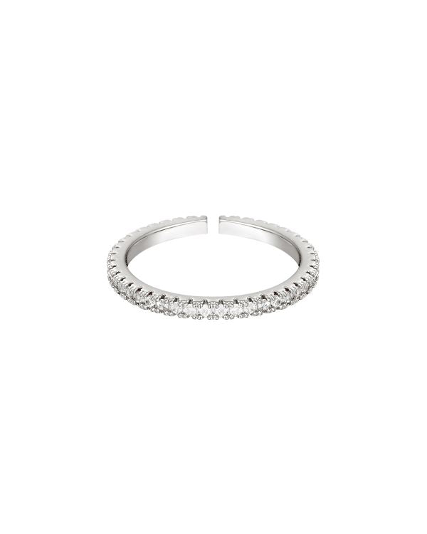 En åben sølvring med indlagte, klare sten langs kanten, ligger centralt mod en hvid baggrund. Ringen er glitrende og elegant i sit design.